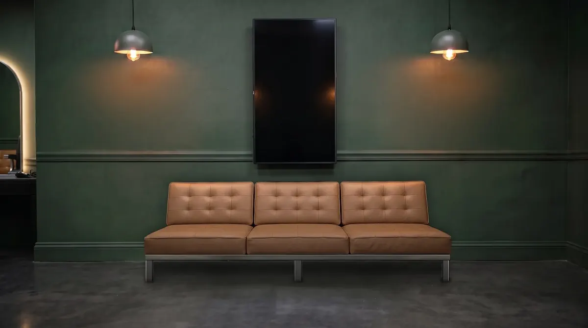A dark green wall with a wall TV and a caramel tufted leather couch below it