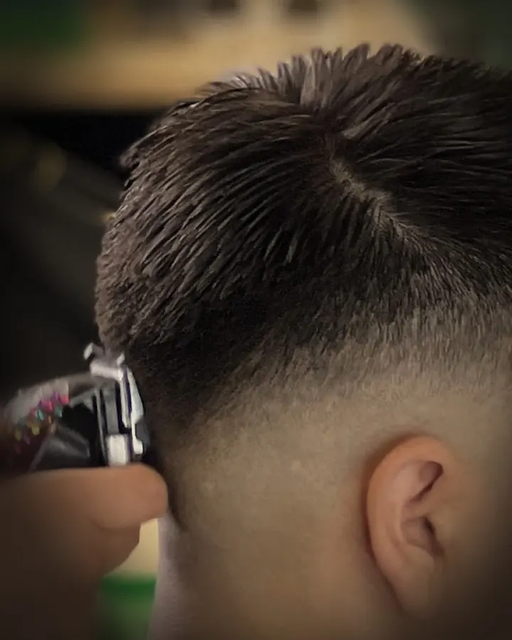 A barber detailing a skin fade at the temple with a clipper